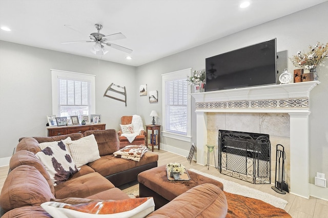 living room featuring light wood-type flooring, a tiled fireplace, ceiling fan, and plenty of natural light