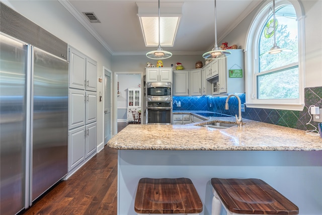 kitchen with built in appliances, light stone counters, kitchen peninsula, dark hardwood / wood-style floors, and decorative backsplash