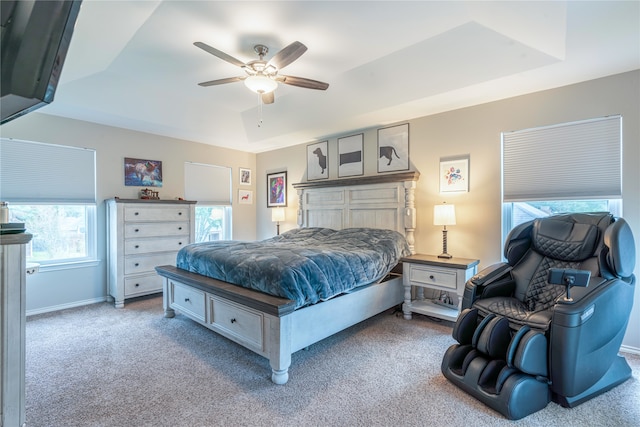 carpeted bedroom featuring a tray ceiling, multiple windows, and ceiling fan