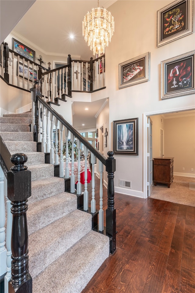 stairway with a towering ceiling, wood-type flooring, a chandelier, and ornamental molding