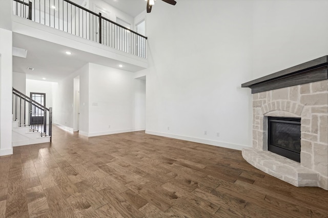 unfurnished living room featuring a fireplace, wood-type flooring, a towering ceiling, and ceiling fan