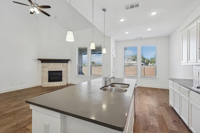 kitchen with pendant lighting, dark wood-type flooring, a center island with sink, sink, and white cabinetry