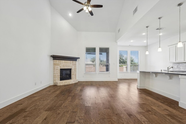 unfurnished living room featuring high vaulted ceiling, a stone fireplace, ceiling fan, and dark wood-type flooring