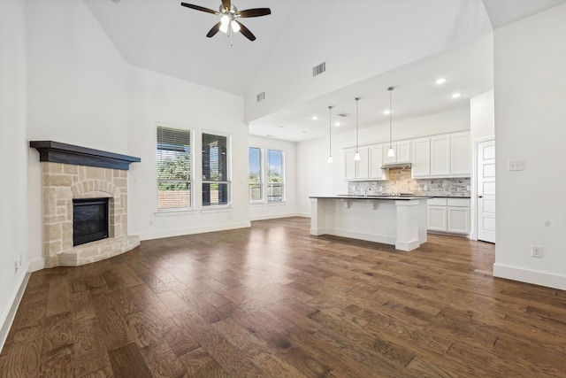 unfurnished living room with a stone fireplace, ceiling fan, high vaulted ceiling, and dark wood-type flooring