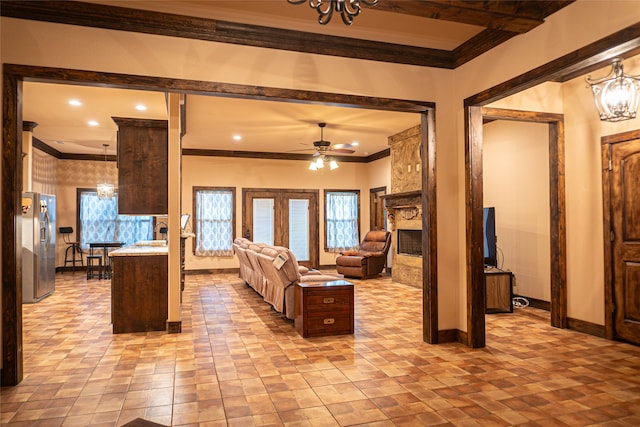 living room with ceiling fan with notable chandelier, plenty of natural light, a stone fireplace, and ornamental molding