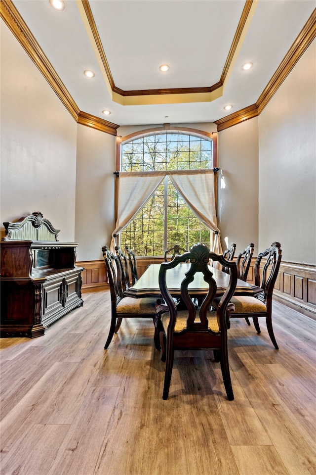 dining space featuring light wood-type flooring, ornamental molding, and a raised ceiling