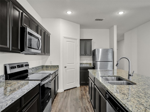 kitchen with stainless steel appliances, light stone countertops, sink, and hardwood / wood-style floors