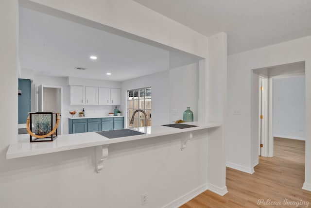 kitchen with sink, kitchen peninsula, a breakfast bar area, white cabinets, and light wood-type flooring