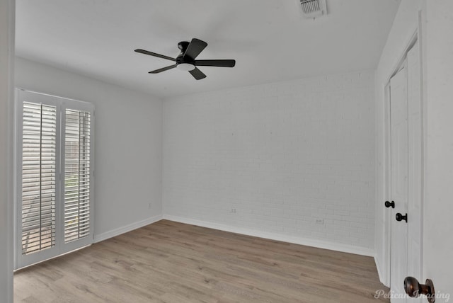 empty room featuring ceiling fan, brick wall, and light hardwood / wood-style flooring