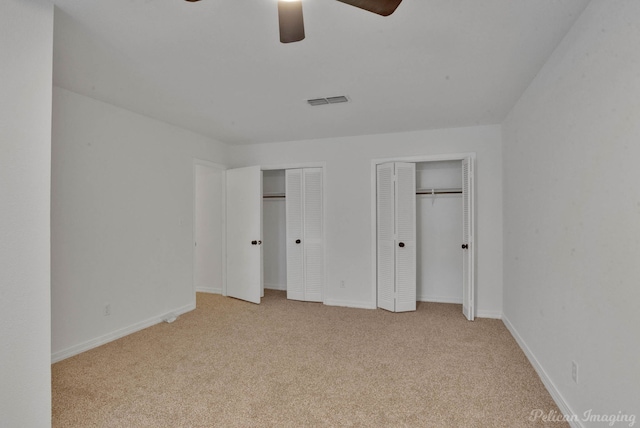 unfurnished bedroom with multiple closets, light carpet, and ceiling fan