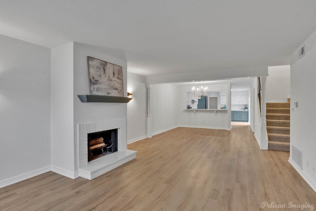 unfurnished living room with light wood-type flooring, a chandelier, and a fireplace