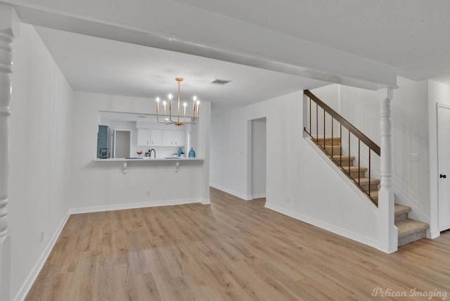 unfurnished living room with an inviting chandelier, sink, and light wood-type flooring