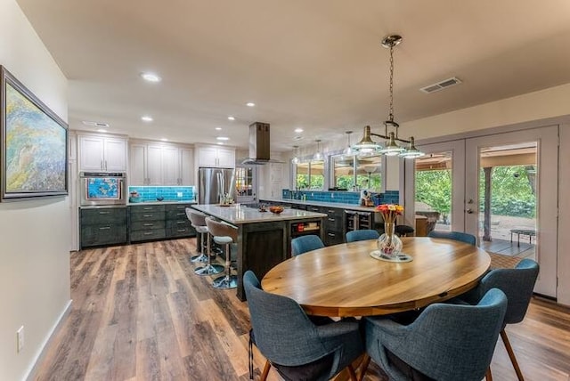 kitchen with stainless steel dishwasher, decorative backsplash, light hardwood / wood-style floors, a large island, and island range hood