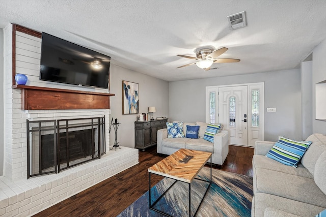 living room featuring a brick fireplace, dark wood-type flooring, a textured ceiling, and ceiling fan