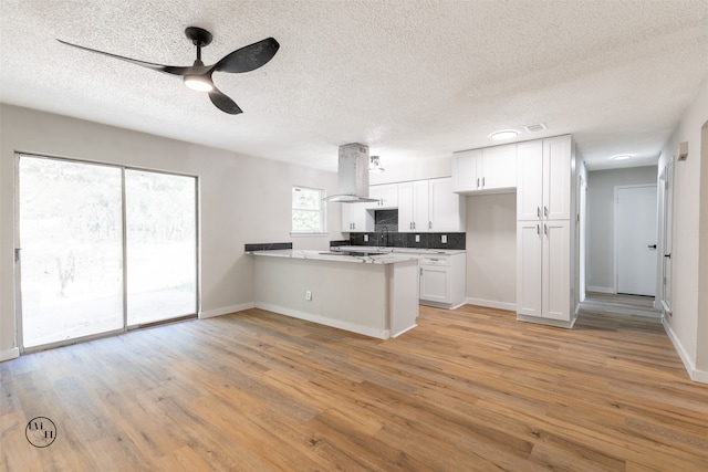 kitchen featuring island exhaust hood, white cabinetry, light wood-type flooring, a textured ceiling, and kitchen peninsula