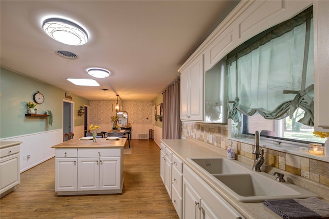 kitchen featuring white cabinetry, light hardwood / wood-style floors, sink, and decorative light fixtures