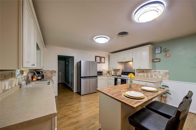 kitchen with a kitchen bar, sink, kitchen peninsula, stainless steel appliances, and white cabinets