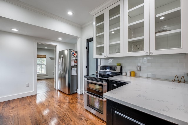 kitchen featuring light stone countertops, appliances with stainless steel finishes, white cabinetry, wood-type flooring, and decorative backsplash