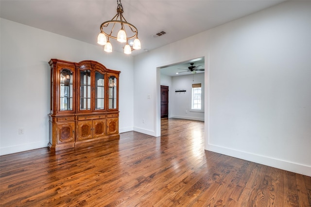 unfurnished dining area with ceiling fan with notable chandelier and dark wood-type flooring