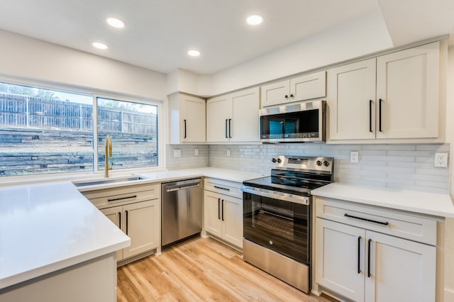 kitchen with light hardwood / wood-style floors, sink, appliances with stainless steel finishes, and tasteful backsplash