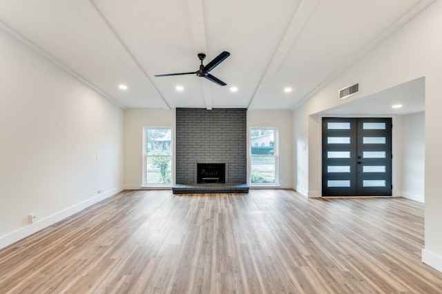 unfurnished living room featuring lofted ceiling with beams, ceiling fan, light hardwood / wood-style flooring, a brick fireplace, and french doors