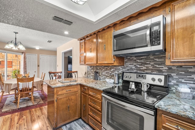 kitchen featuring kitchen peninsula, light wood-type flooring, a textured ceiling, stainless steel appliances, and pendant lighting