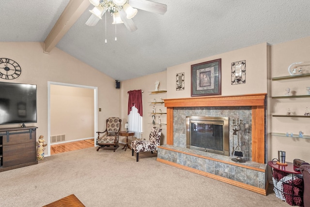 living room with a textured ceiling, carpet floors, ceiling fan, a fireplace, and vaulted ceiling with beams