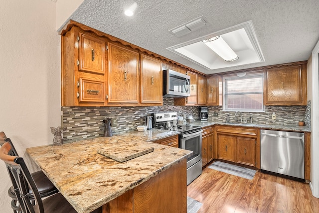 kitchen with a kitchen bar, kitchen peninsula, a textured ceiling, and appliances with stainless steel finishes