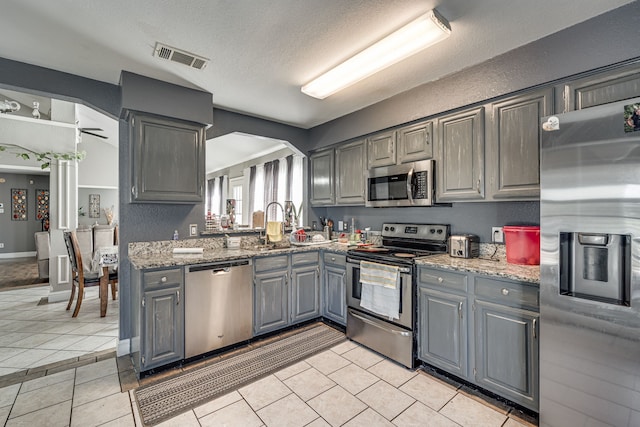 kitchen with gray cabinetry, appliances with stainless steel finishes, a textured ceiling, light stone countertops, and ceiling fan