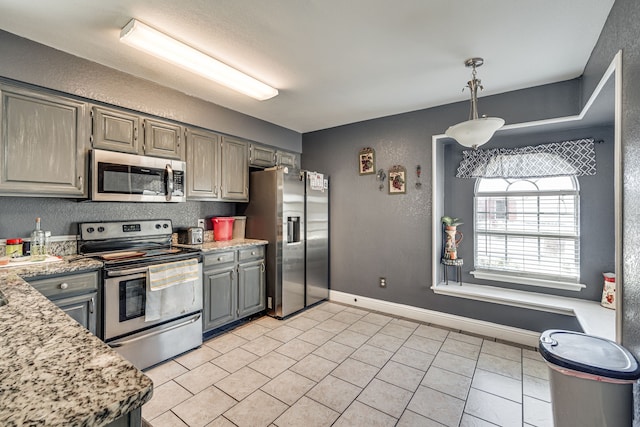 kitchen with appliances with stainless steel finishes, hanging light fixtures, light stone counters, and gray cabinetry