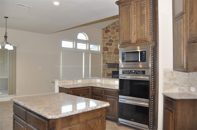 kitchen with a kitchen island, light stone countertops, hanging light fixtures, and stainless steel appliances