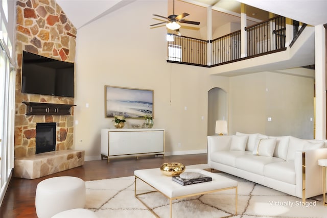 living room featuring a stone fireplace, high vaulted ceiling, dark hardwood / wood-style floors, and ceiling fan