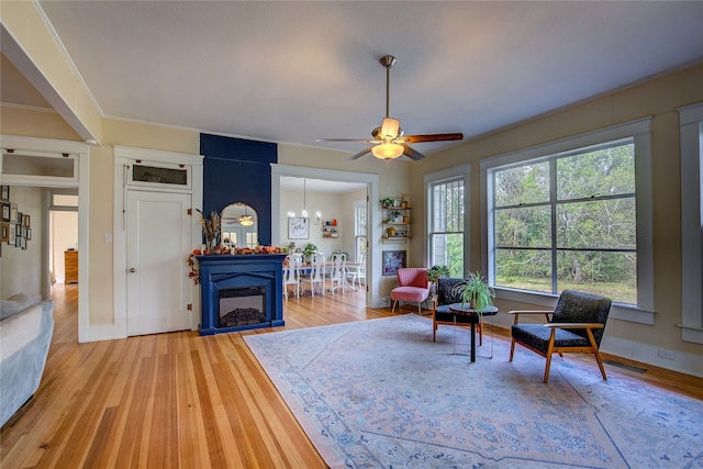 living room featuring ornamental molding, ceiling fan with notable chandelier, a large fireplace, and light hardwood / wood-style flooring