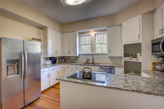 kitchen with stainless steel appliances, white cabinetry, sink, light stone countertops, and light wood-type flooring