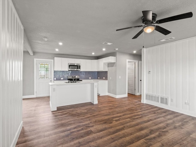 kitchen featuring appliances with stainless steel finishes, a textured ceiling, hardwood / wood-style floors, a kitchen island with sink, and white cabinets