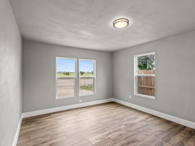 empty room featuring plenty of natural light, light wood-type flooring, and a textured ceiling