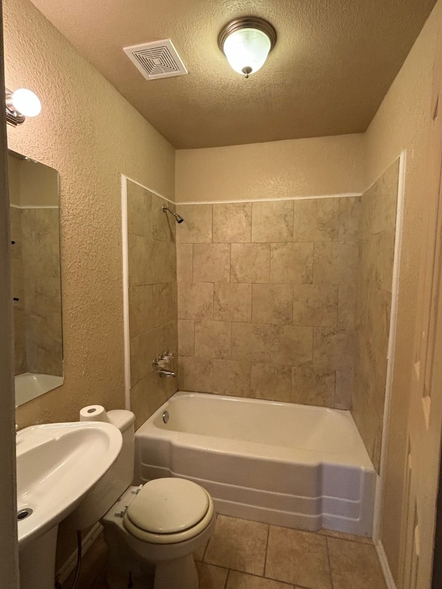 bathroom featuring tile patterned flooring, a textured ceiling, toilet, and tiled shower / bath combo