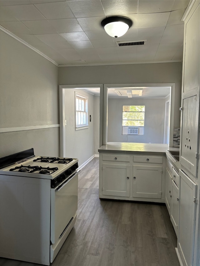 kitchen featuring crown molding, white cabinetry, white gas range, dark hardwood / wood-style flooring, and kitchen peninsula