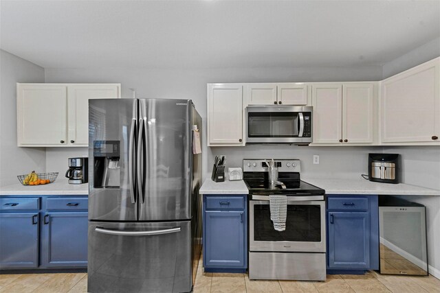 kitchen with white cabinets, blue cabinetry, light tile patterned flooring, and appliances with stainless steel finishes