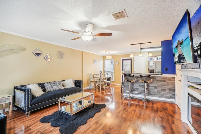 living room with ceiling fan, wood-type flooring, a textured ceiling, and crown molding