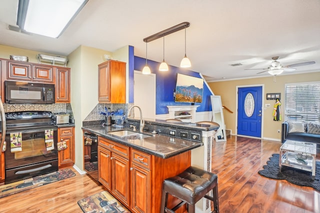 kitchen featuring light hardwood / wood-style floors, sink, a breakfast bar, black appliances, and kitchen peninsula