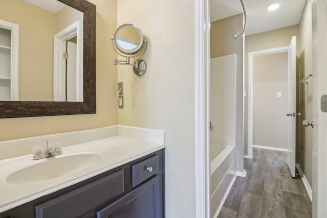 bathroom with baseboards, shower / bathing tub combination, wood finished floors, and vanity