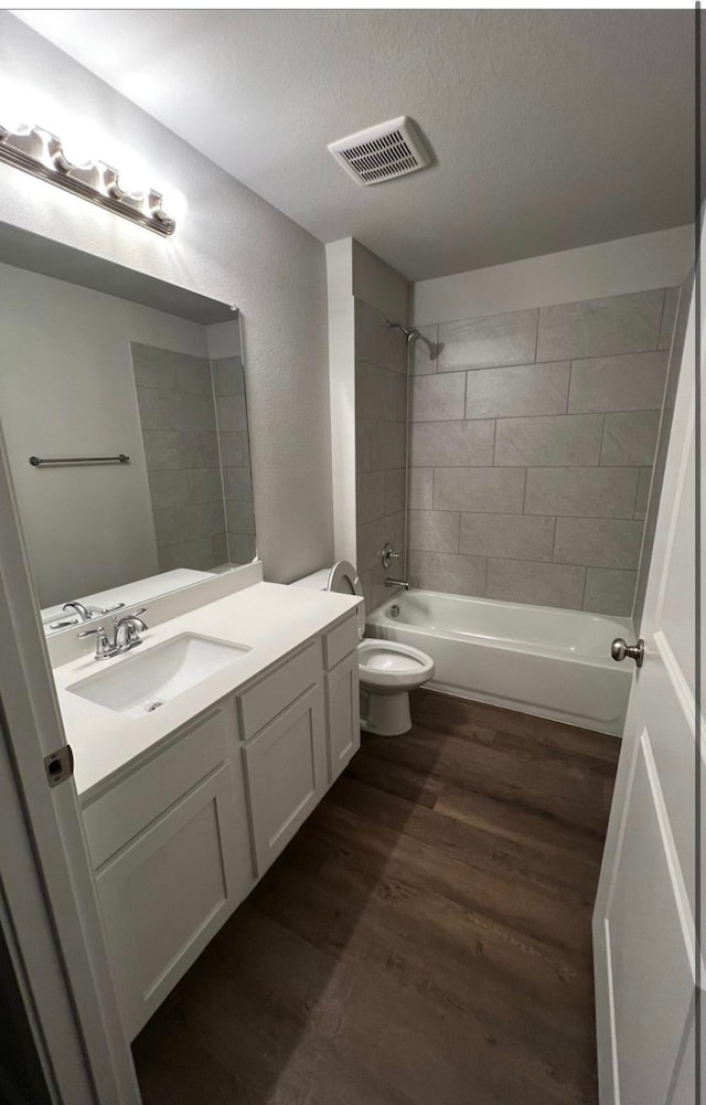 full bathroom with wood-type flooring, a textured ceiling, toilet, vanity, and tiled shower / bath