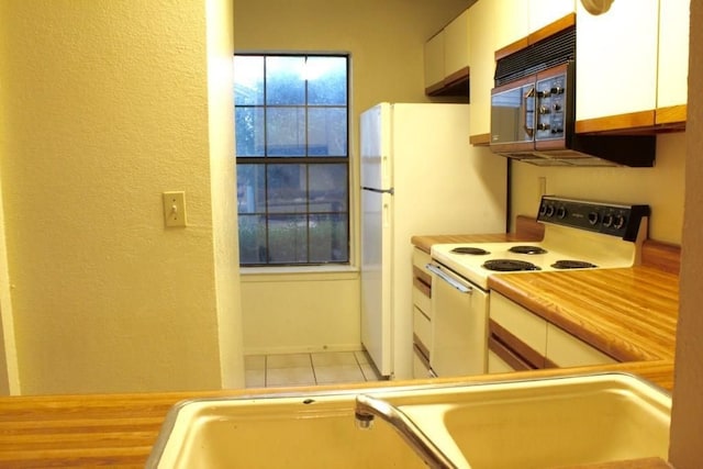 kitchen featuring white electric range oven, white cabinets, light tile patterned floors, and sink