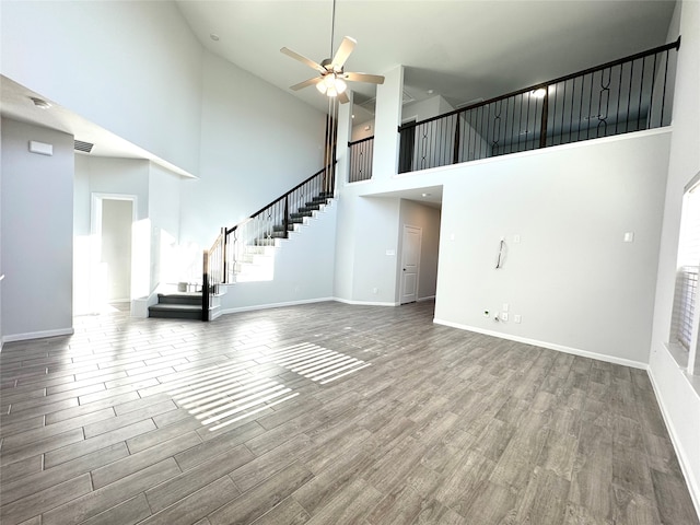 unfurnished living room with a high ceiling, wood-type flooring, and ceiling fan