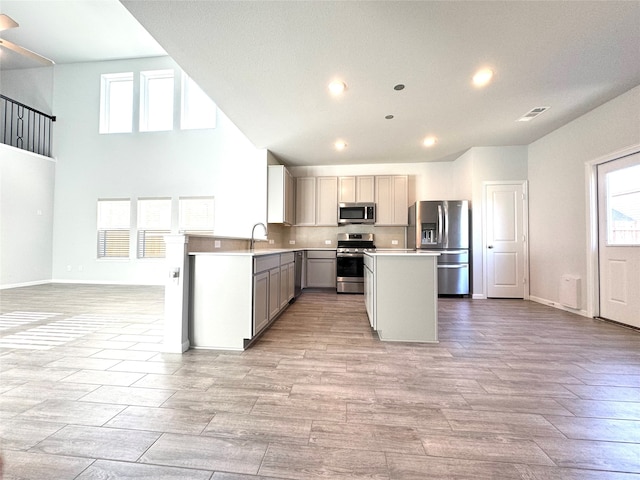 kitchen featuring sink, appliances with stainless steel finishes, a towering ceiling, gray cabinets, and light wood-type flooring