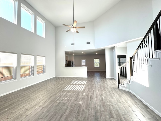 unfurnished living room with hardwood / wood-style floors, a towering ceiling, and ceiling fan