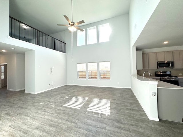 unfurnished living room with sink, hardwood / wood-style floors, ceiling fan, and a towering ceiling