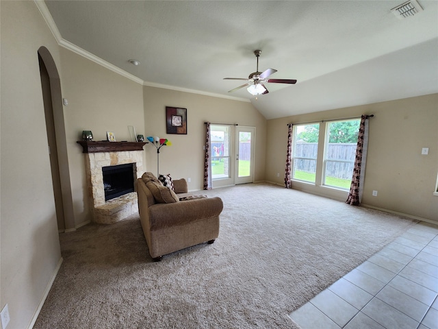 living room with a stone fireplace, light tile patterned floors, ceiling fan, and crown molding