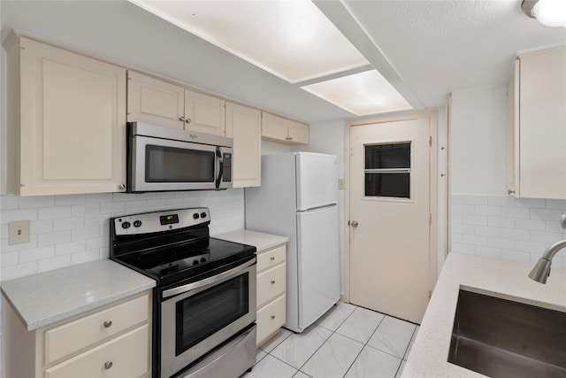 kitchen featuring tasteful backsplash, sink, cream cabinetry, and stainless steel appliances